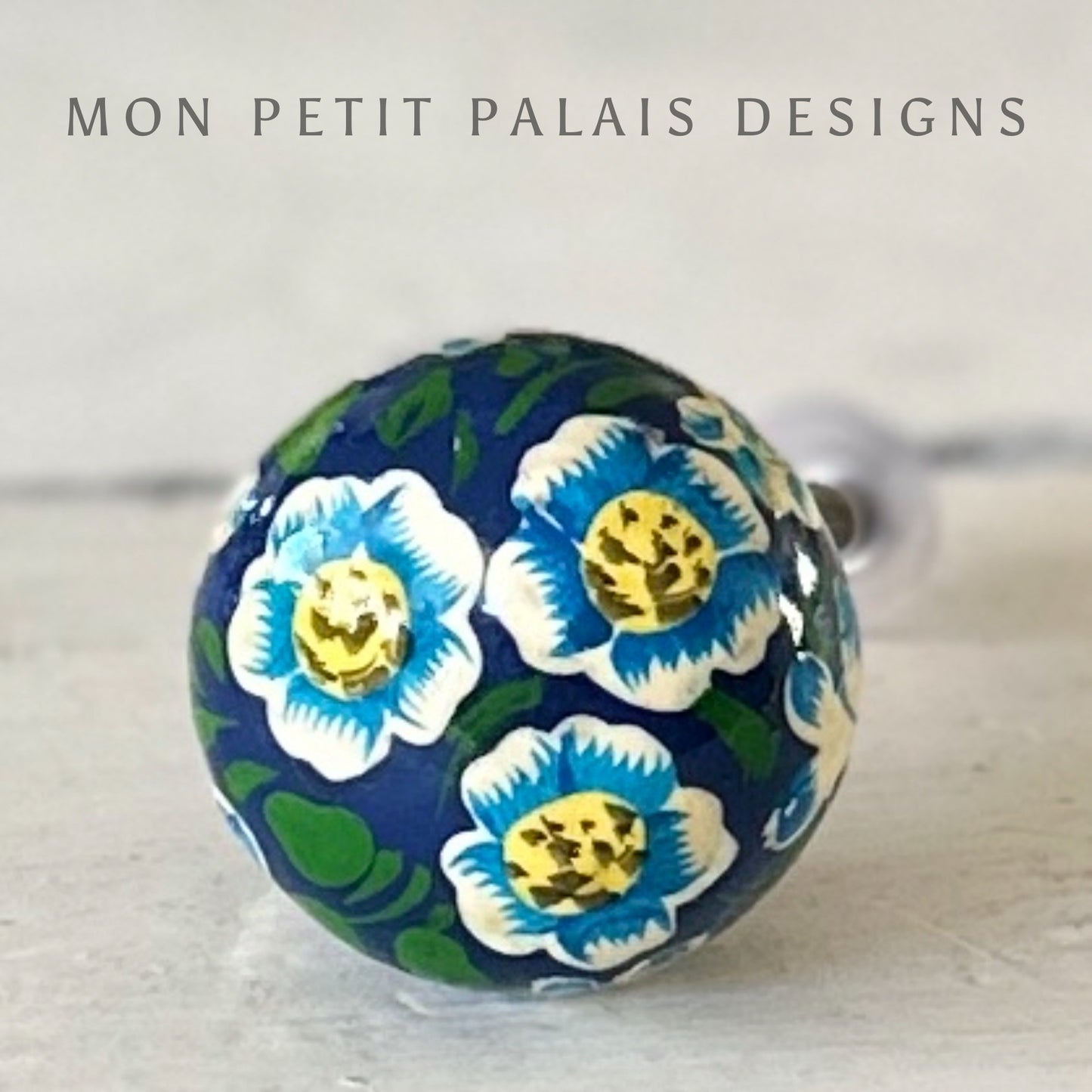 A decorative spherical knob with a floral design in blue, green, and white colors, branded by MON PETIT PALAIS DESIGNS.