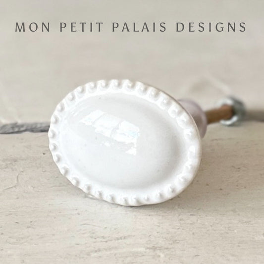 A white vintage ceramic knob with an oval shape and raised detail edge.