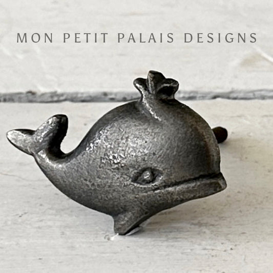 A pewter-colored iron cabinet knob shaped like a little whale, with the brand 'MON PETIT PALAIS DESIGNS' visible.