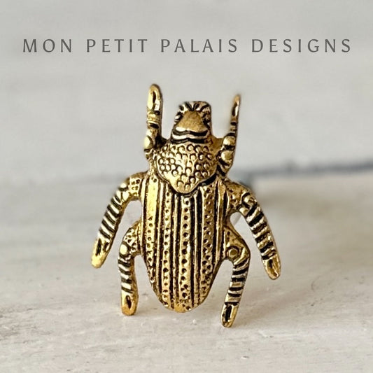 A gold-colored metal door knob designed to resemble a scarab, with intricate patterns and details on its surface.