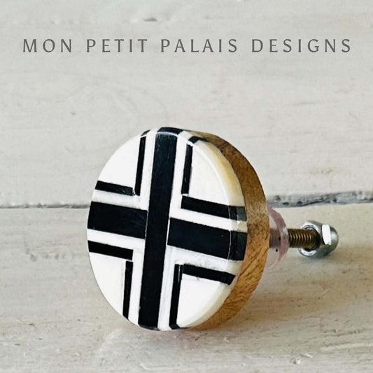 A round black and cream bone inlay knob with a cross design, attached to a furniture piece.