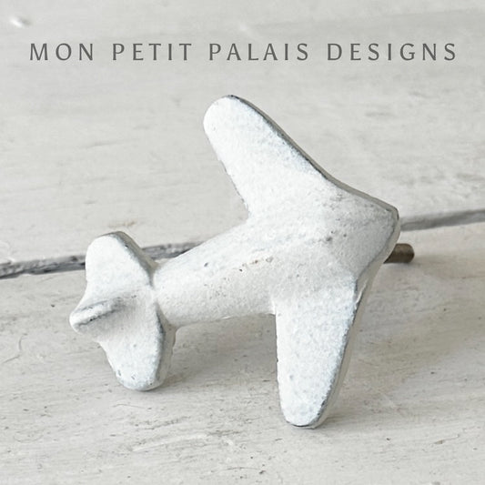 A white vintage metal knob designed to resemble an aeroplane, with a textured surface, mounted on a flat surface.