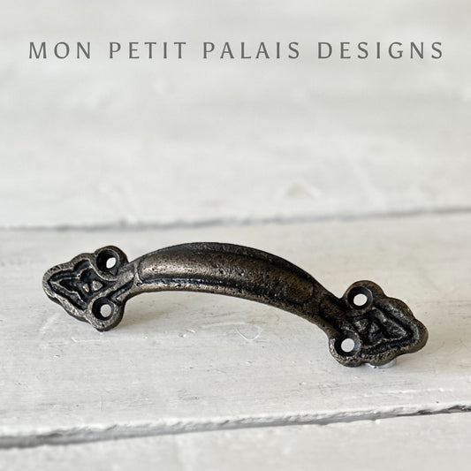 A  metal bar handle with a brass finish, displayed against a white wooden background.