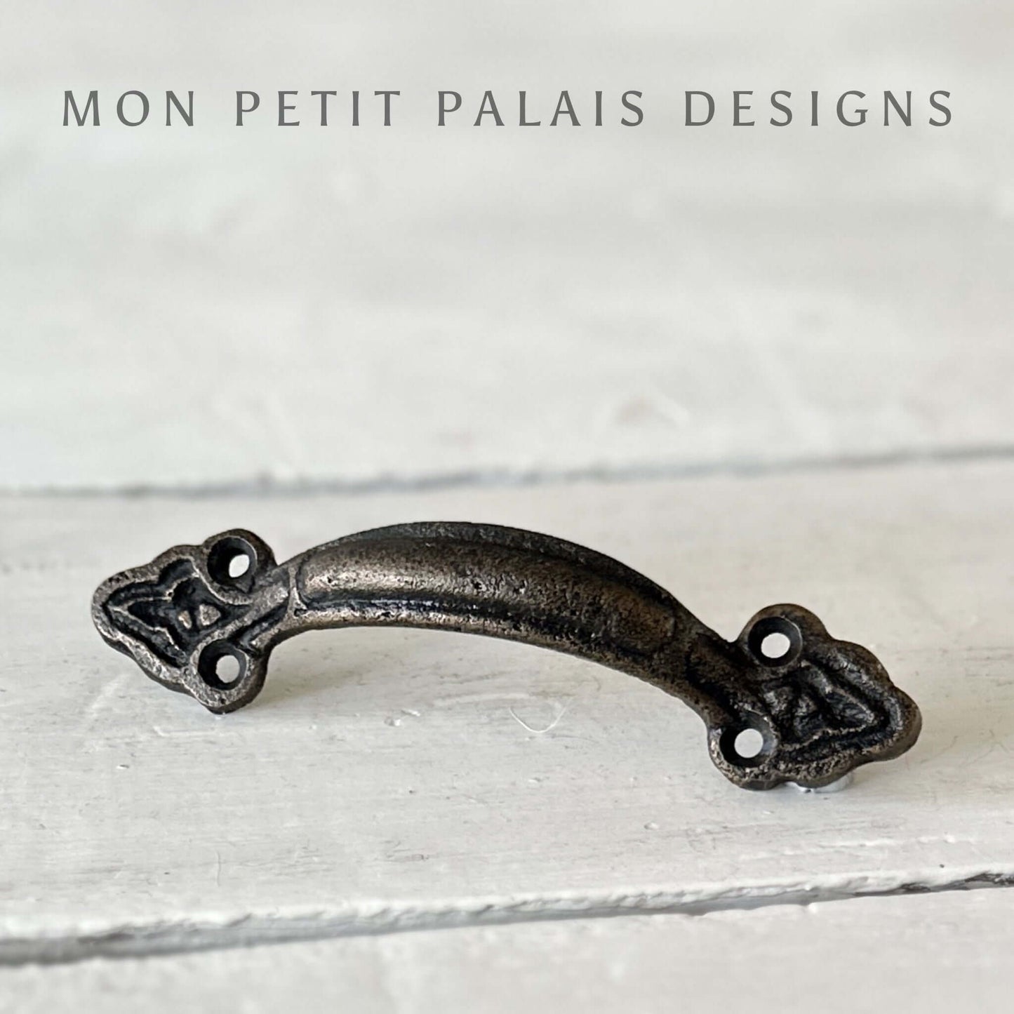 A metal bar handle with a brass finish, displayed against a white wooden background.