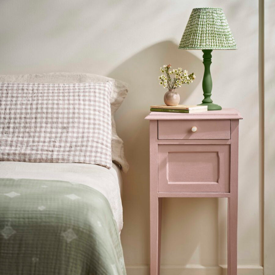 Bedroom scene featuring a Jaipur Pink painted bedside table beside a bed dressed in check and neutral linens.