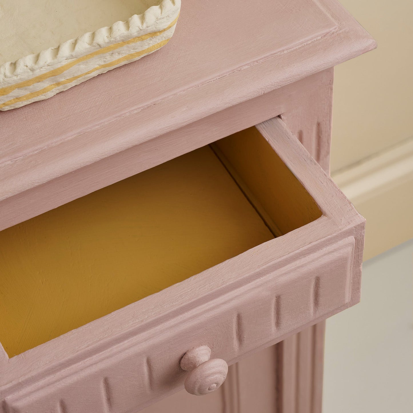 Detail of drawer interior on a Jaipur Pink painted bedside cabinet, showing contrast between soft pink and warm yellow interior.