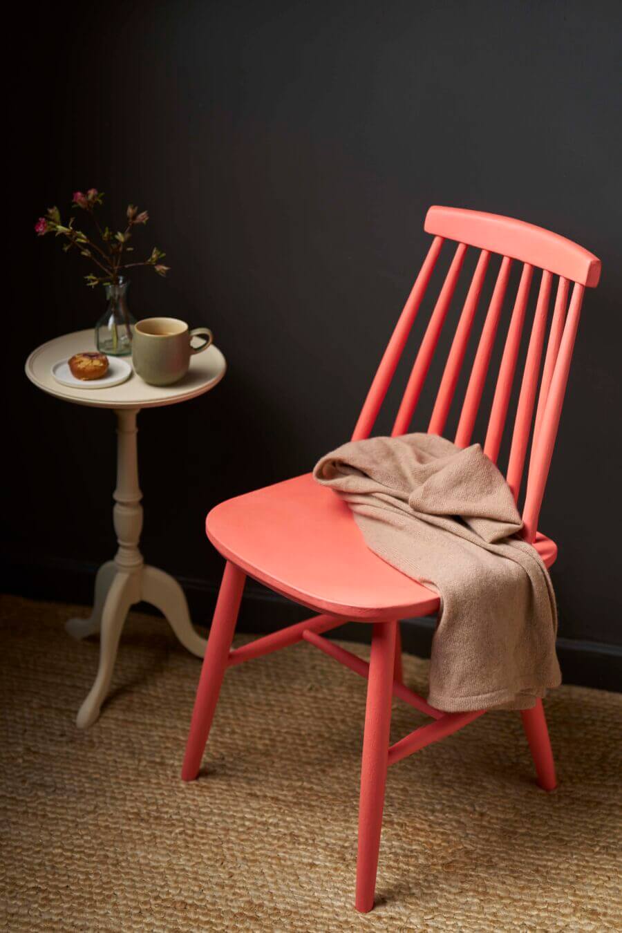 Wooden chair painted in Sandalwood Red Chalk Paint, styled with a throw, side table, and dark backdrop.