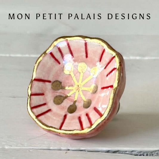 Blush and gold bloom ceramic knob close-up with red detail and gold edges.