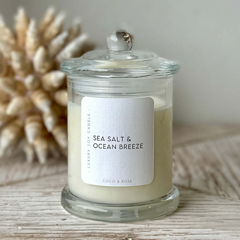 Candle labeled 'Sea Salt & Ocean Breeze' on a wooden surface with a blurred natural background