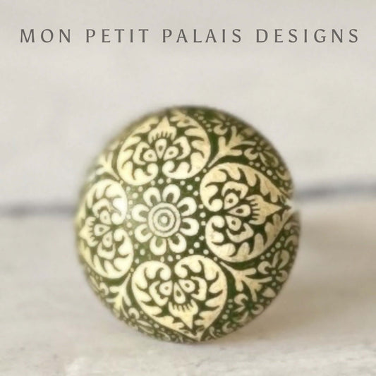 A round engraved cabinet knob with a geometric pattern in gold and green colors against a white background.