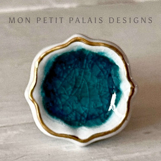 A sea foam green and white crackle glass knob with gold accents, displayed against a neutral background.