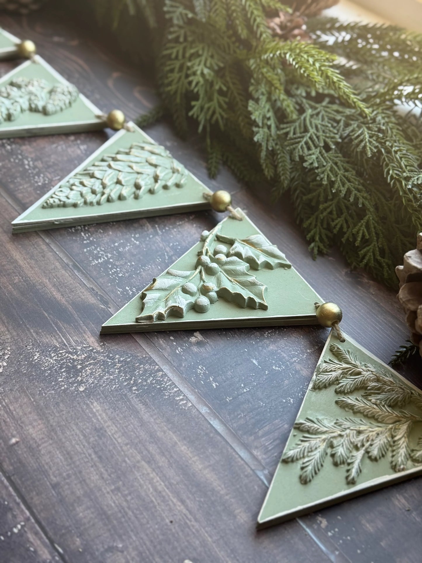 IOD Winter Forage Decor Mould™ decorative elements featuring pinecones and foliage on a rustic wooden surface.
