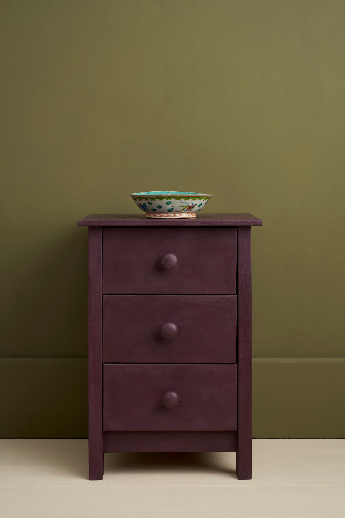Purple dresser with three drawers against a green wall