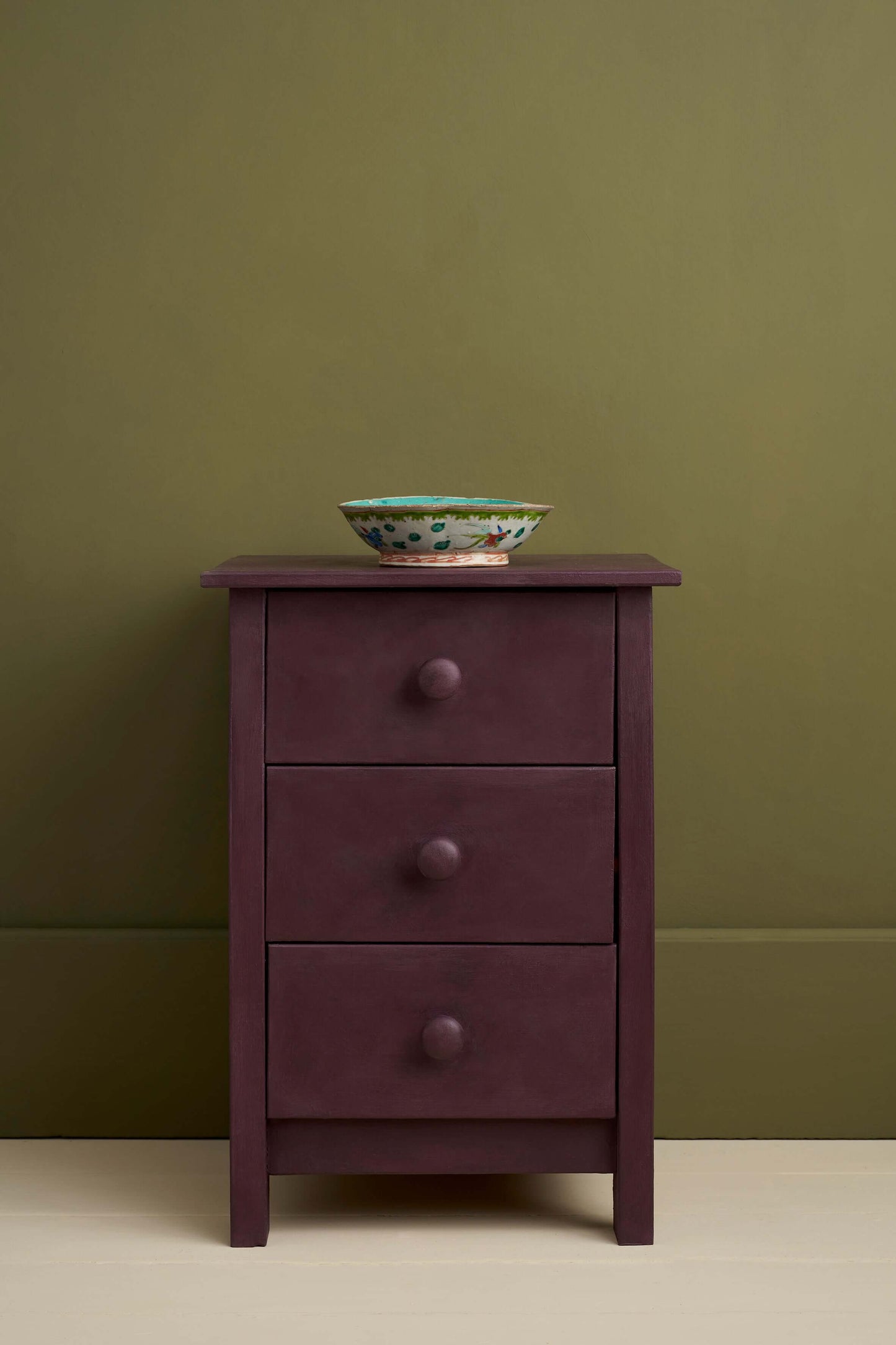 Purple dresser with three drawers against a green wall