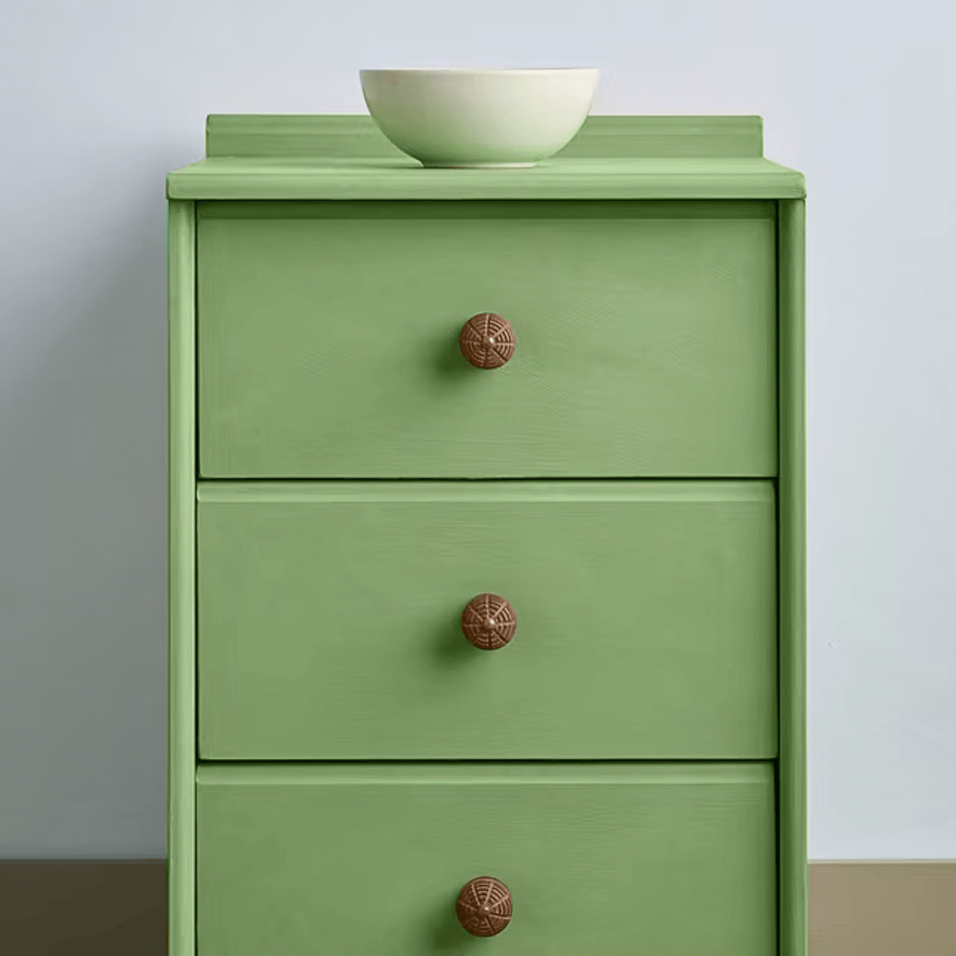 Capability Green Annie Sloan Chalk Paint used on a three-drawer dresser with wooden knobs and a bowl on top.