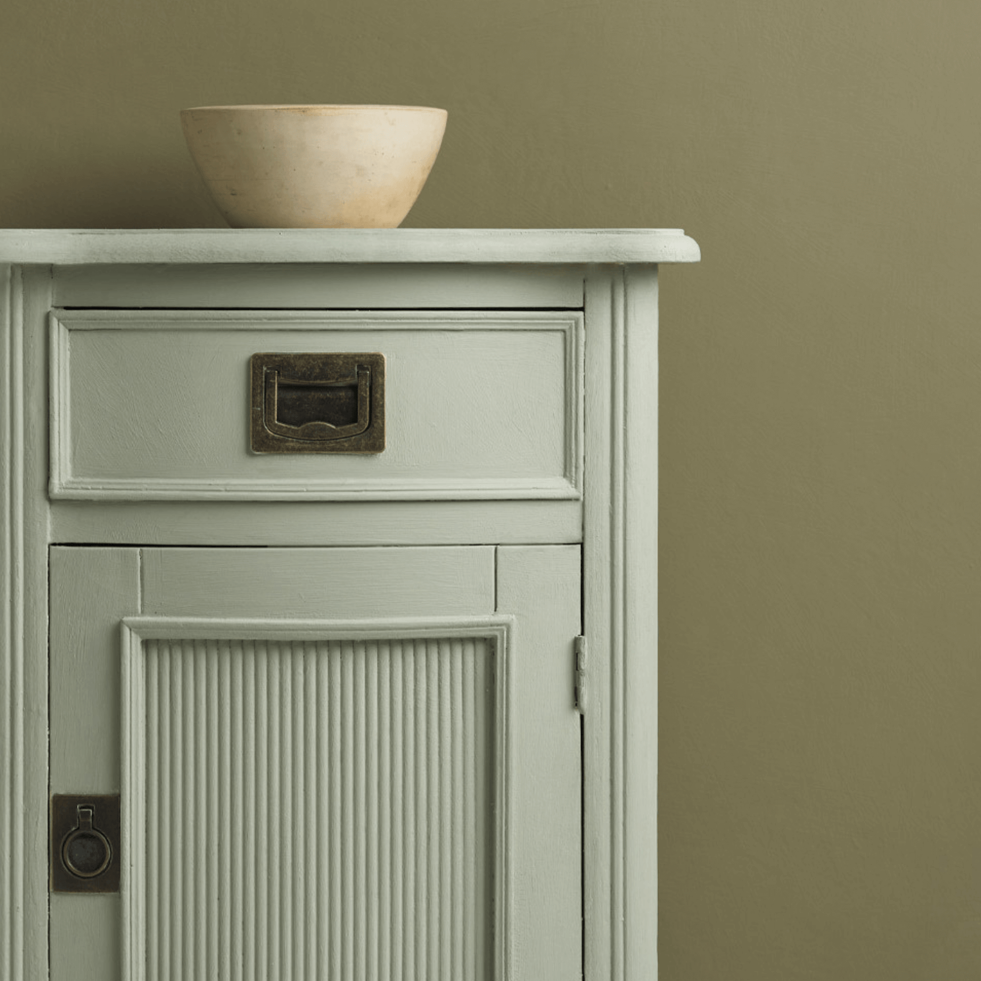 Coolabah Green Annie Sloan Chalk Paint on a cabinet with a bowl against a muted background.
