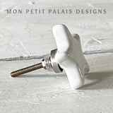 Side view of a white ceramic star knob with metal accents for furniture.