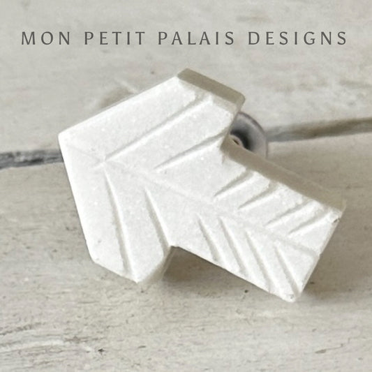 A white marble cabinet knob with an arrow design.