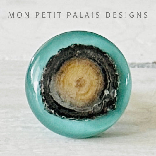 A seafoam green wooden and resin knob with visible wood grain and a black and beige design detail.