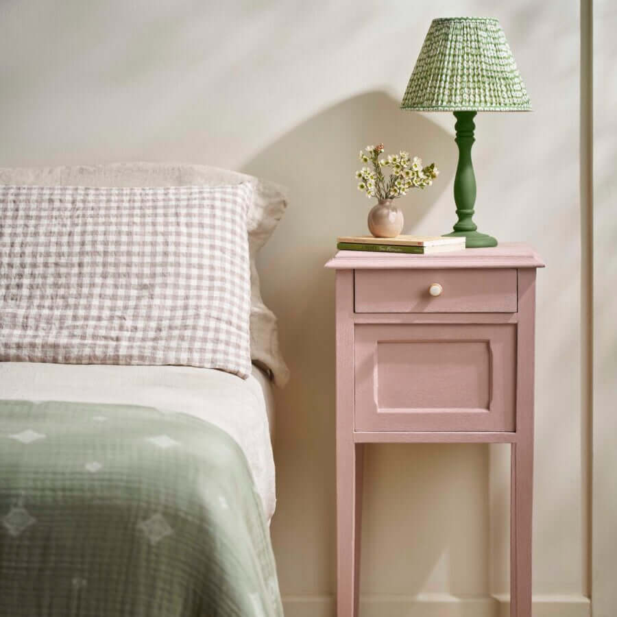 Bedroom scene featuring a Jaipur Pink Annie Sloan Chalk Paint bedside table beside a bed dressed in check and neutral linens.