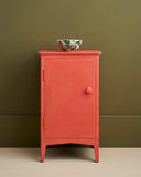 Small cabinet fully painted in Annie Sloan Sandalwood Red against an olive green wall, styled with a ceramic bowl.