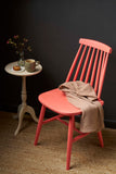 Wooden chair painted in Sandalwood Red Chalk Paint, styled with a throw, side table, and dark backdrop.