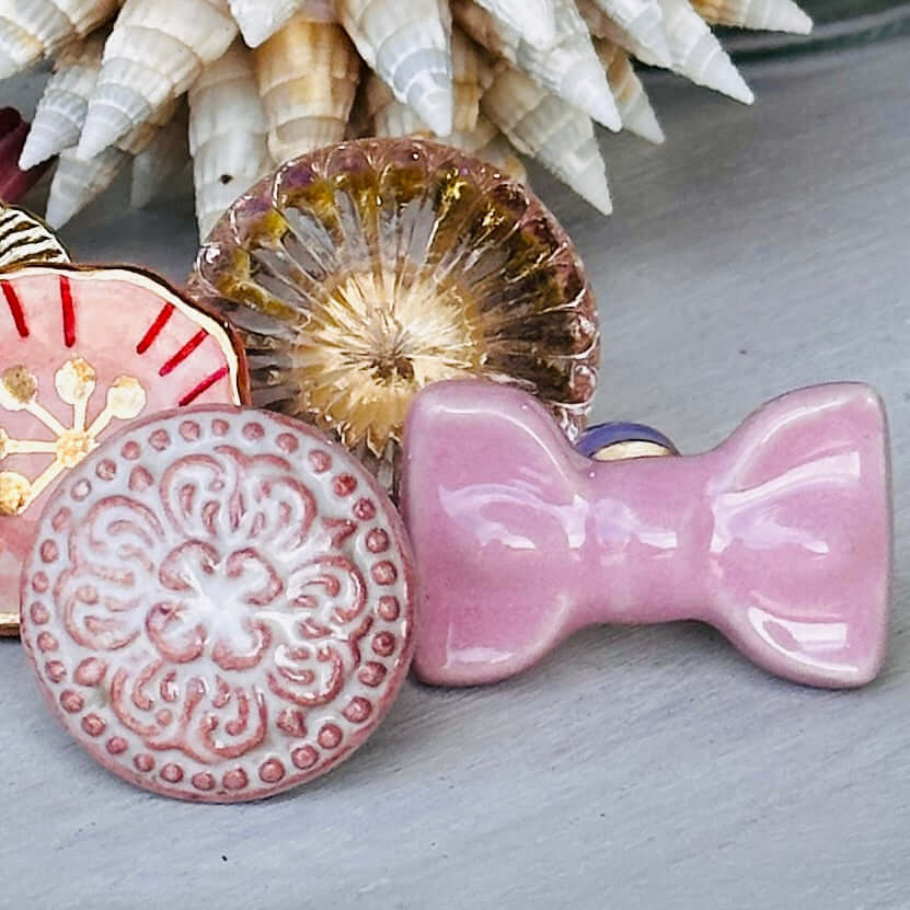 Pink Ceramic Bow Cabinet Knob and decorative ceramic knobs on a wooden surface.