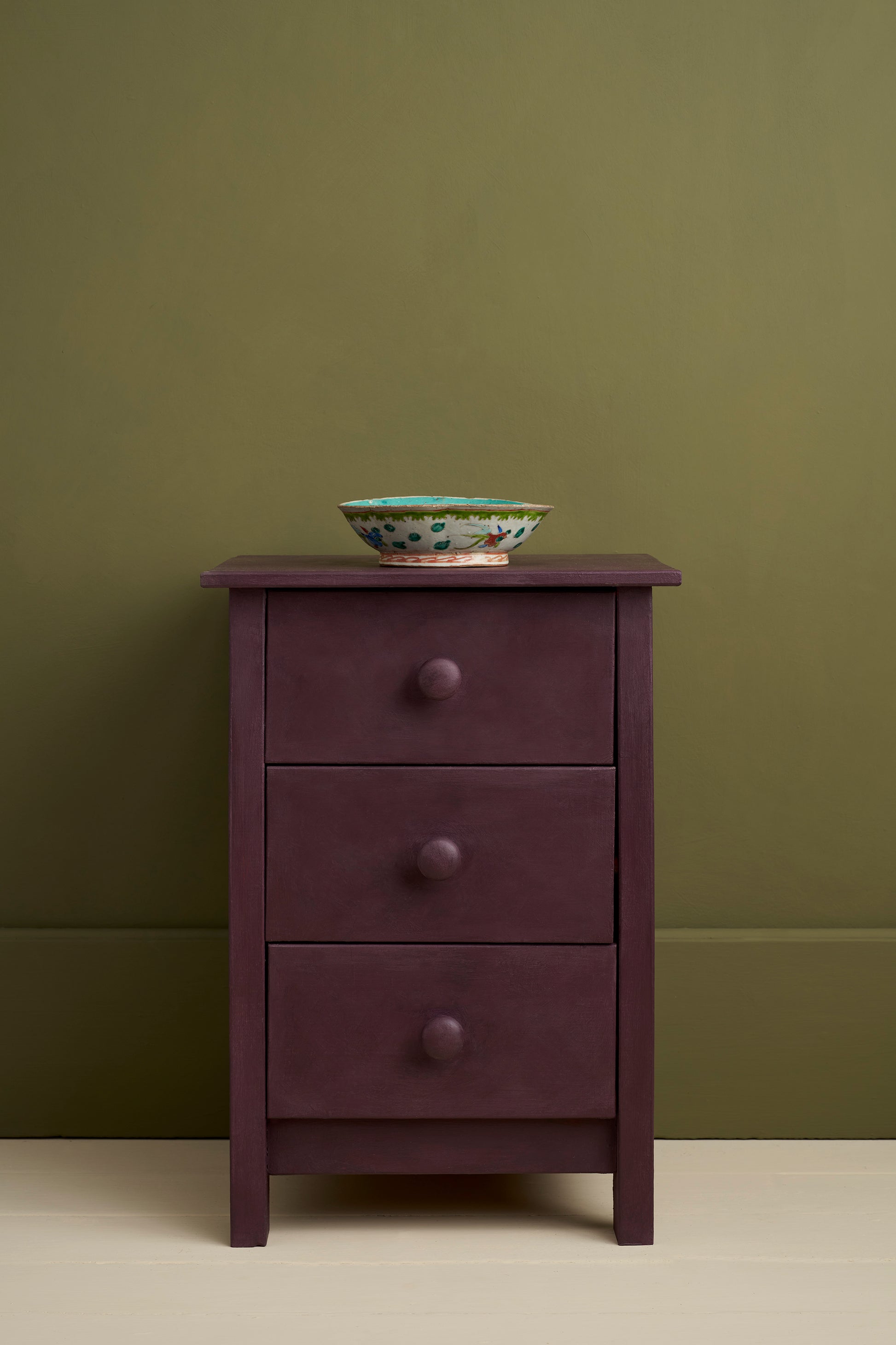 Purple dresser with three drawers against a green wall