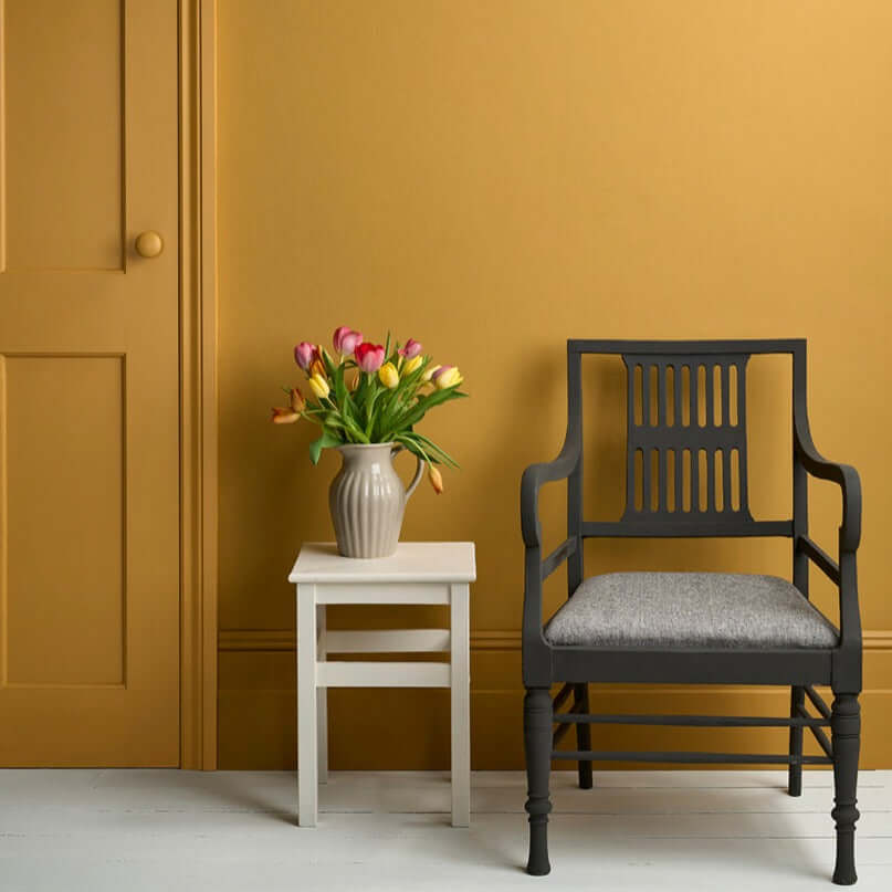 Carnaby Yellow - Annie Sloan Satin Paint used on a wall with a black chair and a vase of tulips.