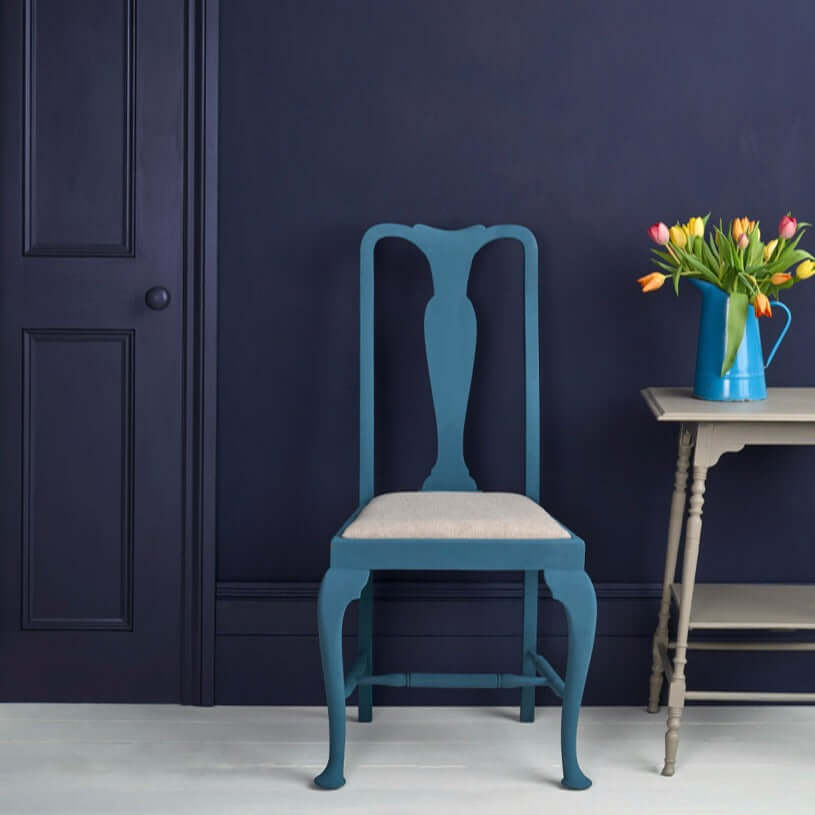 A stylish chair painted in Oxford Navy - Annie Sloan Satin Paint against a dark wall, with a vase of tulips.